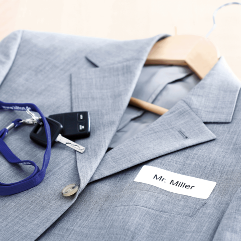 Grau blazer mit einem Namensschild "Mr. Miller", einem Schlüsselbund und einem Schlüsselanhänger auf einem Holzständer.