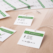 Modeetiketten mit Größenangaben und Farboptionen in grünem und weißem Design auf einem Holzuntergrund.