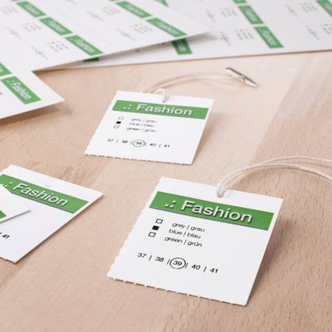 Modeetiketten mit Größenangaben und Farboptionen in grünem und weißem Design auf einem Holzuntergrund.