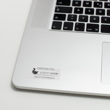 Ein Laptop mit einer Tastatur und einem Aufkleber, der "EIGENTUM VON paperswan" und "NICHT ENTFERNEN" zeigt.