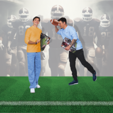 Zwei junge Männer stehen auf einem Fußballfeld. Einer hält einen Football, der andere zeigt Daumen hoch und hält Zeitschriften. Im Hintergrund sind Fußballspieler zu sehen.