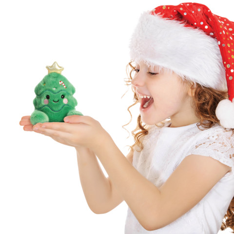 Ein Mädchen mit einem Weihnachtsmann-Hut hält ein grünes, lächelndes Plüschweihnachtsbaumspielzeug in den Händen.