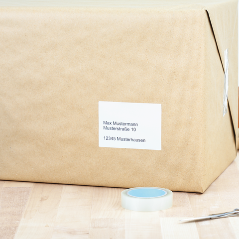 Ein Ordner mit beschrifteten Fächern für eingehende und ausgehende Dokumente steht auf einem Tisch, daneben liegen Umschläge und eine Postkarte.