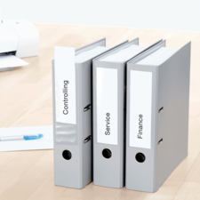 Drei graue Ordner mit Beschriftungen: "Controlling", "Service" und "Finance", auf einem Schreibtisch neben einem Stift und einem Drucker.