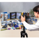 Eine Person fotografiert eine Vielzahl von Büro- und Bastelmaterialien, darunter Ordner, Kleber und Bastelwerkzeuge, auf einem Tisch.