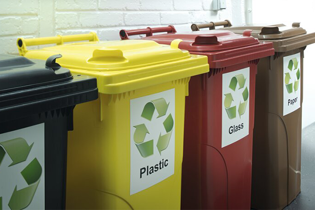 Fläschchen mit Flüssigkeiten, verschiedene Abfallbehälter für das Recycling und eine Person, die ein Warnschild für gefährliche Stoffe anbringt.