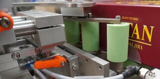 Maschinenteile mit grünen Zylindern und einer roten Verpackung im Hintergrund, die für einen automatisierten Produktionsprozess verwendet werden.