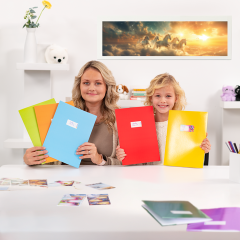 Eine Frau und ein Kind sitzen an einem Tisch, in den Händen halten sie bunte Ordner. Auf dem Tisch liegen Fotos, und im Hintergrund ist ein Bild von Pferden zu sehen.