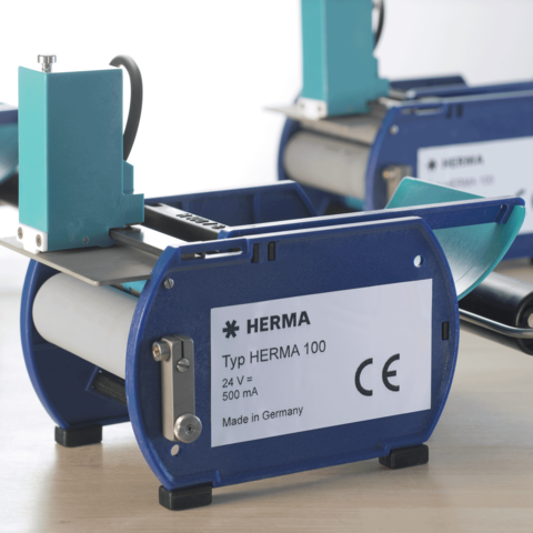 HERMA Typ 100 Etikettiermaschine mit blauer und grauer Gehäusefarbe, 24 V, 500 mA, hergestellt in Deutschland.