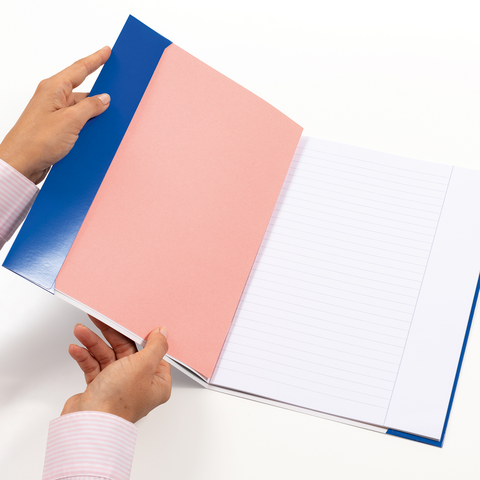 Eine Person hält ein offenes Notizbuch mit blauem Einband, rosa Innenseiten und linierten Blättern.