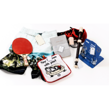 Bunte Shorts, ein Tischtennisschläger, ein Notizbuch, ein Stift, ein Kissen mit Aufschrift und verschiedene andere Gegenstände auf einem weißen Hintergrund.