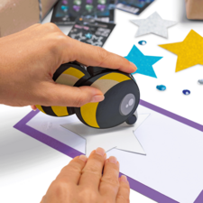 Eine Hand benutzt einen Stempel, um einen Stern auf ein Blatt Papier zu drucken, das von bunten Sternen und Dekorationen umgeben ist.