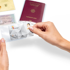Eine Hand hält eine transparente Hülle mit einer ID-Karte, während ein Reisepass und mehrere Dokumente im Hintergrund liegen.