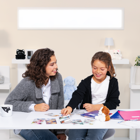 Zwei Mädchen sitzen an einem Tisch, umgeben von Fotos und Notizen, während sie miteinander plaudern und lachen.