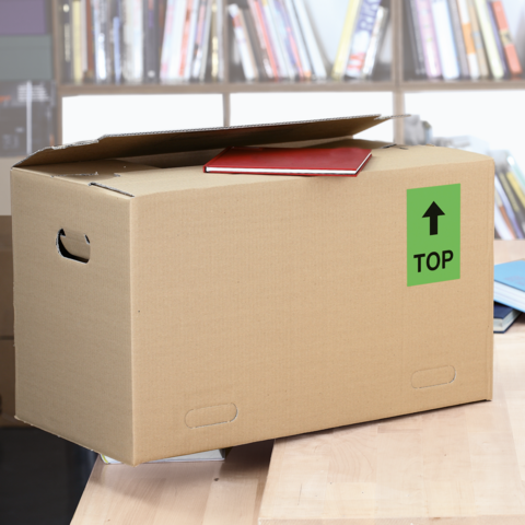 Ein brauner Karton mit dem Aufkleber "FRAGILE", daneben ein graues Kuvert mit "URGEN!T" und eine Schere.