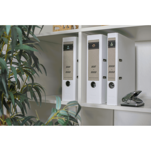 Drei weiße Ordner auf einem Regal, beschriftet mit den Jahren 2020, 2021, 2022 und 2023, neben einem Heftgerät und einer Pflanze.