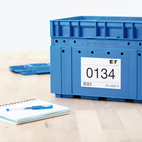 Blaue Kunststoffbox mit einer Etikette, die die Nummer 0134 zeigt, auf einem Tisch neben einem Notizblock und einem Stift.