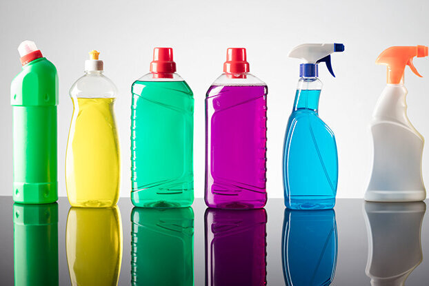 Reihe von Reinigungsmittelflaschen in verschiedenen Farben auf einer reflektierenden Oberfläche.