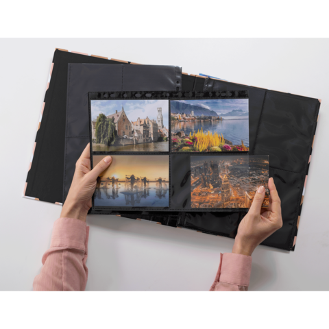Eine Person hält ein Fotoalbum mit vier Bildern, darunter Landschaften und Stadtansichten, in einer hellen Umgebung.